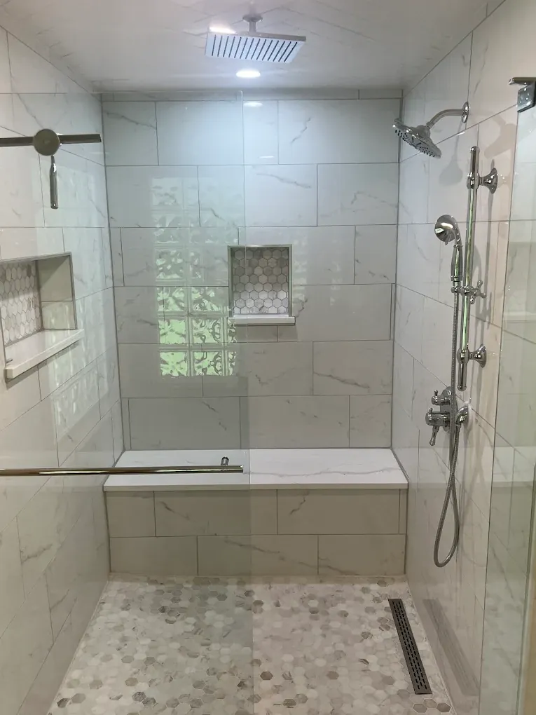 Luxury walk-in marble shower with dual shower heads, bench seat and hex mosaic floor in Loveland, Ohio