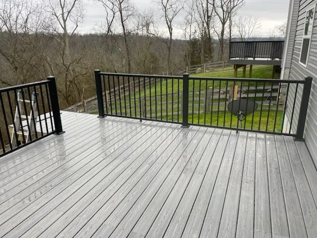 Wide gray composite deck with black metal railing overlooking wooded backyard in Amelia, Ohio by Abrams Restoration