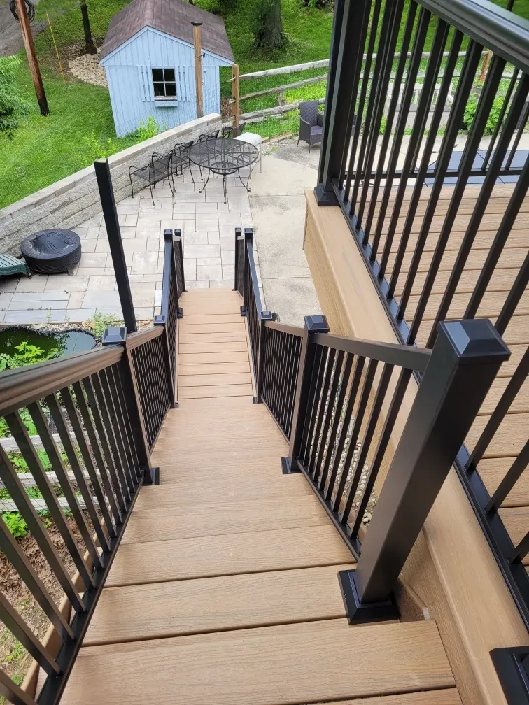 Custom Trex composite deck with black metal railings and staircase to paver patio in Batavia, Ohio by Abrams Restoration