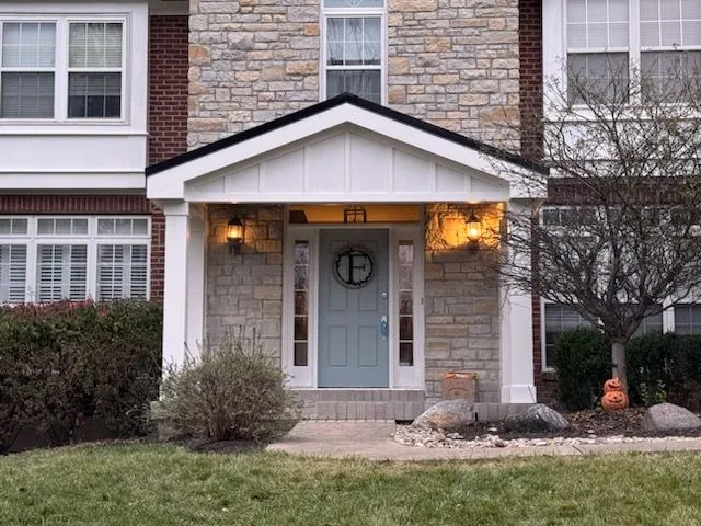 Natural stone facade entry with covered porch, sconce lighting and white trim on a home in Batavia, Ohio