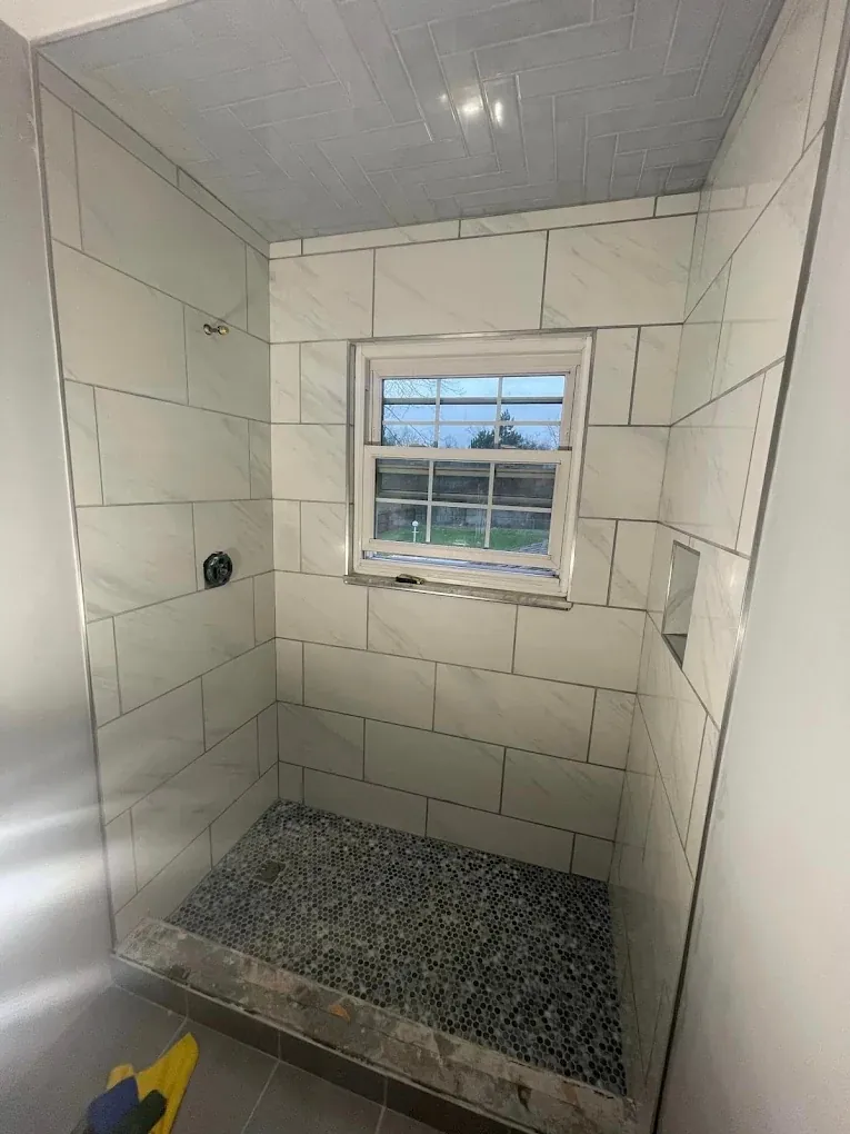 Walk-in tile shower with marble-look walls, pebble mosaic floor and window niche in Cincinnati, Ohio