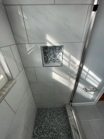 Floor-to-ceiling marble-look tile walk-in shower with mosaic floor and glass door in Batavia, Ohio