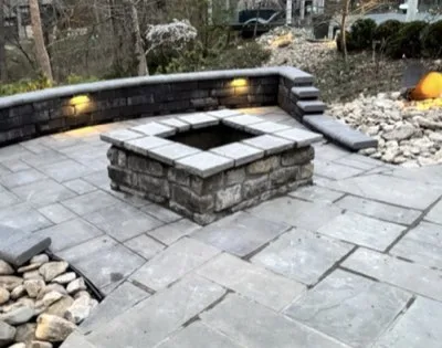 Custom stone fire pit with paver patio, low seat wall and integrated landscape lighting in Loveland, Ohio by Abrams Restoration