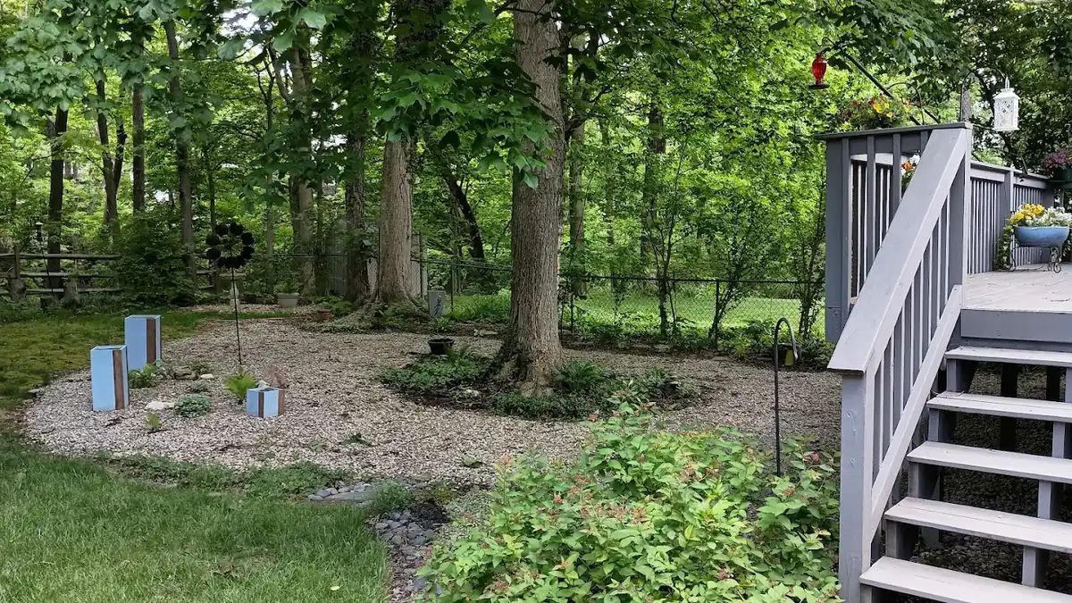 Wooded backyard with pea gravel landscape bed and painted deck staircase in Milford, Ohio